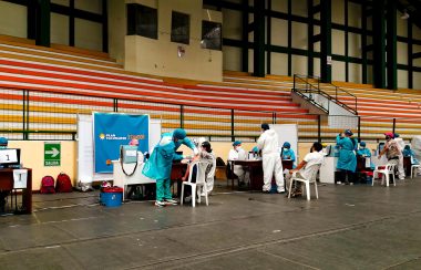 A roll of people sitting down in an arena to receive a needle from a nurse