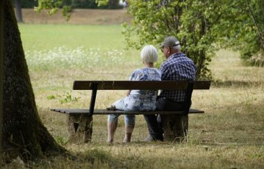 Un couple âgé est assis sur un banc dehors et regarde le paysage.