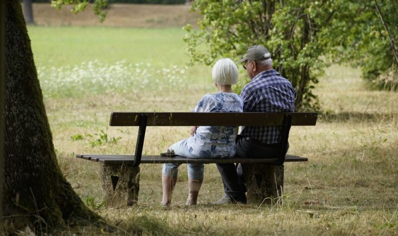 Un couple âgé est assis sur un banc dehors et regarde le paysage.