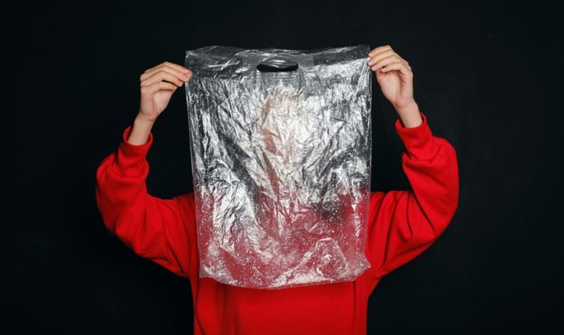 Personne portant un chandail rouge tenant un sac de plastique devant leur visage.