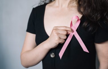 A person is seen holding an arm up across their chest, a pink ribbon held in their hand over their chest.