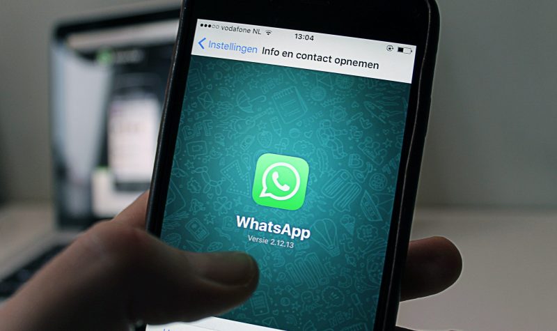 A hand holding up a cell phone showing the whatsapp logo