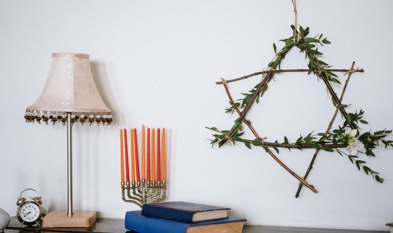 A series of items, including a Menorah, have been placed on a brown table. There is also a lamp, and a handmade Star of David hangs from the wall.