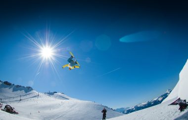 A snowboarder performs a jump, caught in this photo mid air against a blue sky