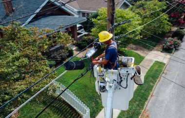 A man repairs power lines high up off the ground.