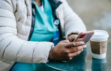 Stock photo of a health looking professional in scrubs holding a phone on her hand looking at some app.