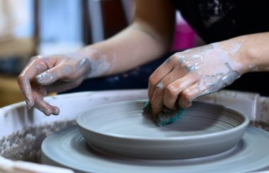 A closeup of a potter's hands while working with clay, appearing to make a plate out of clay