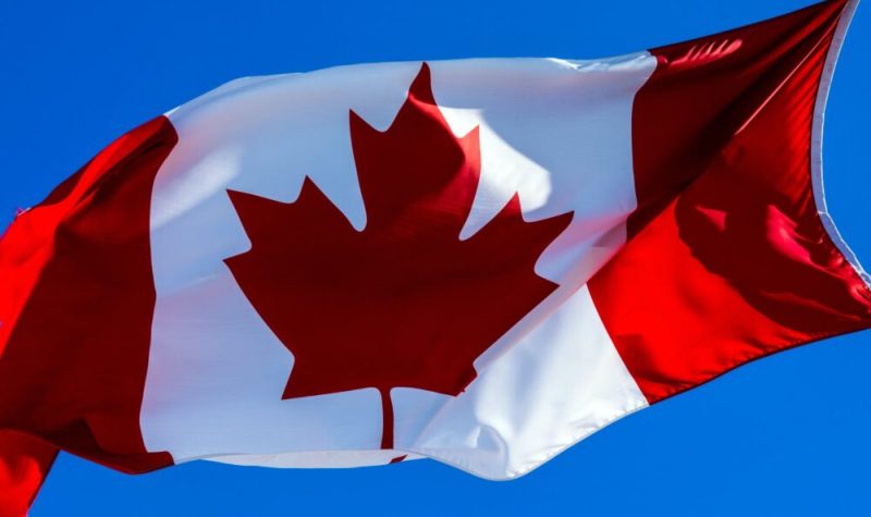 Un gros drapeau du Canada en blanc ert rouge contre un ciel bleu.