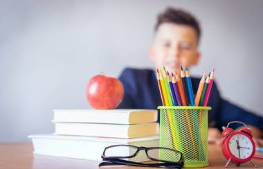 Lunettes, livres, pomme et crayons sur un pupître avec élève en arrière plan.