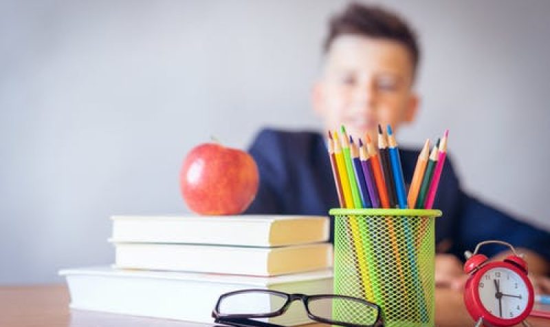 Lunettes, livres, pomme et crayons sur un pupître avec élève en arrière plan.