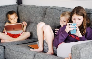 Des jeunes enfants assis sur un sofa regardant des tablettes.