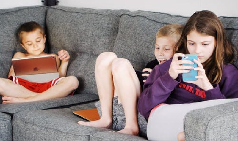 Des jeunes enfants assis sur un sofa regardant des tablettes.
