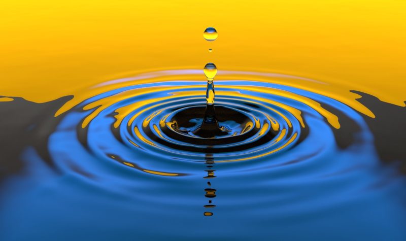 A water droplet creating a ripple in a body of water. The top half of the water is tinted yellow and the bottom half of the water has a blue darker tint.