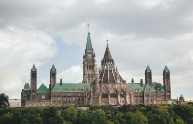 The Parliament buildings in Ottawa are seen over a forested hill top.