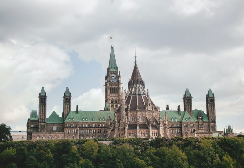The Parliament buildings in Ottawa are seen over a forested hill top.