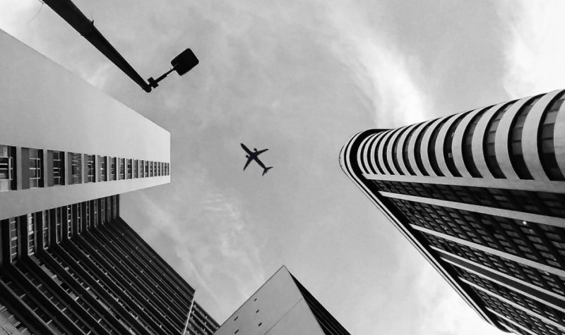 Un avion volant dans un ciel gris entouré de bâtiments.