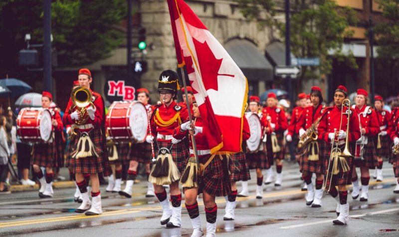Une fanfare, vêtue de rouge, des instruments à la main, avec le drapeau canadien au vent.