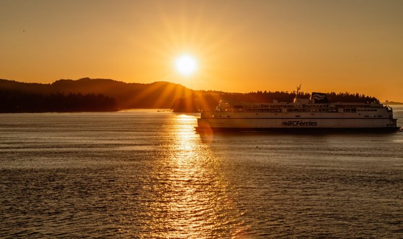 A BC Ferries vessel sails against a sunlit background.