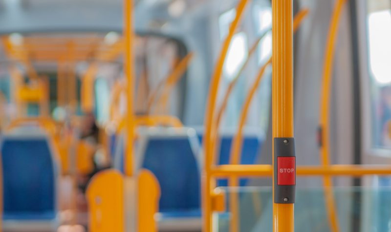 Photo of the inside of a public transit bus, the seats are blue and the handle bars are yellow. There is a red stop button.
