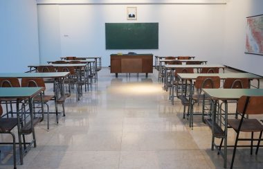 Student desks lined up on either side of a classroom in front of a chalkboard.