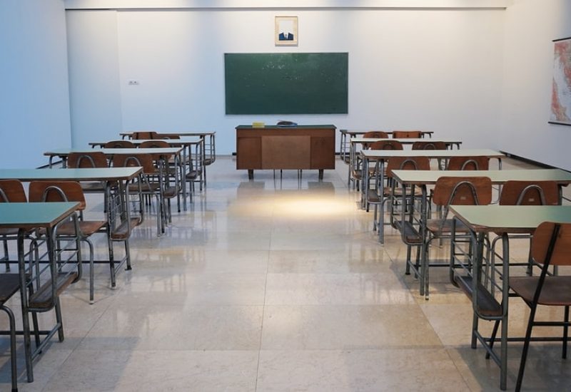 Student desks lined up on either side of a classroom in front of a chalkboard.