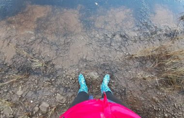 Le bas du corps et les pieds d'une personne portant des bottes de pluie bleues debout dans de la boue
