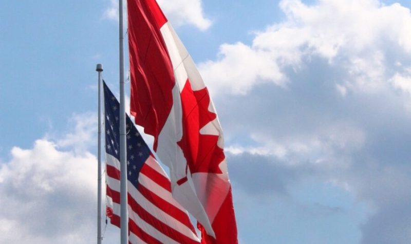 Un drapeau du Canada et un drapeau des États-Unis photographié dans un ciel bleu et quelques nuages.