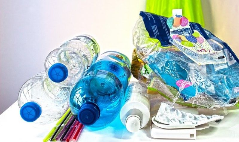 Bouteilles en plastiques, emballages de plastique et pailles en plastiques sur une table blanche dans une pièce aux murs blancs.