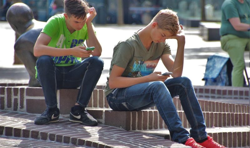 Deux jeunes garçons en position assises chacun avec un cellulaire à la main