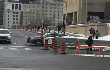 A provincial police vehicle is seen parked behind a police barricade while traffic moves past.
