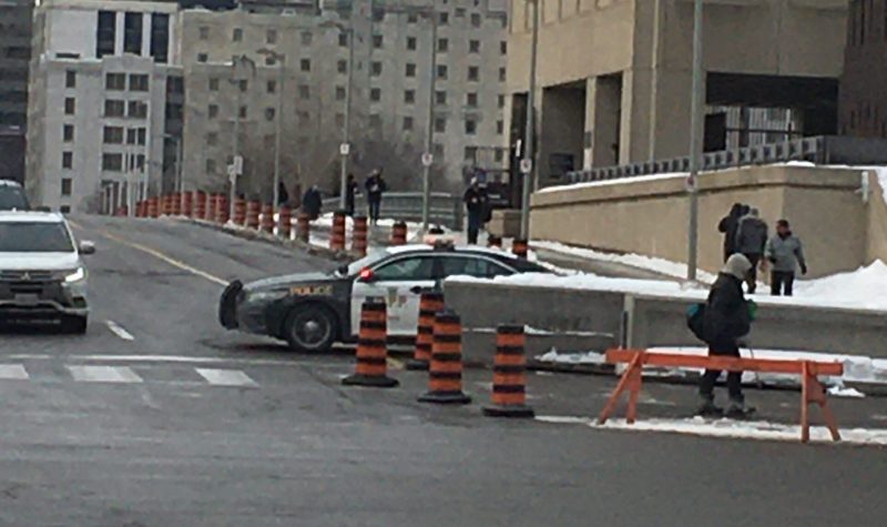 A provincial police vehicle is seen parked behind a police barricade while traffic moves past.