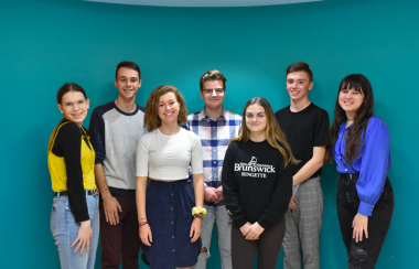 7 adolescents qui font partie de la Fédération des jeunes francophones du Nouveau-Brunswick (FJFNB) sont debout devant un arrière-plan bleu.