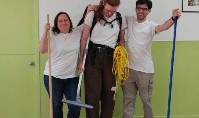 Three members of Powerhouse Co-Op wear matching white T-shirts and are holding cleaning equipment.