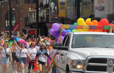 People are seen marching behind the truck with baloons and colours for Halifax's 2022 Pride Parade.