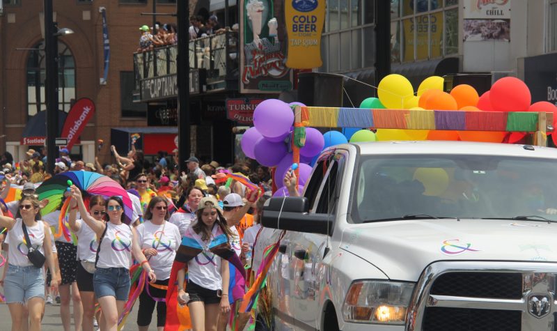 People are seen marching behind the truck with baloons and colours for Halifax's 2022 Pride Parade.