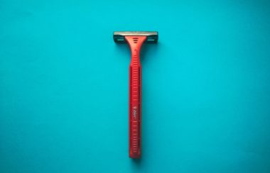 A red disposable razor sits on a light blue background.