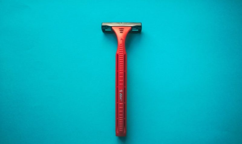 A red disposable razor sits on a light blue background.
