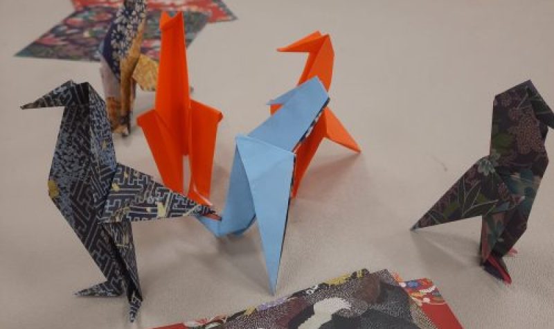 Six origami ravens sit on a table along with stacks of origami paper.