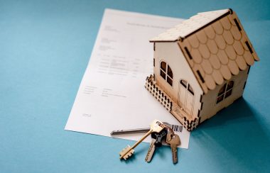 A model house and a pair of keys lie on top of a document sitting on a table top.