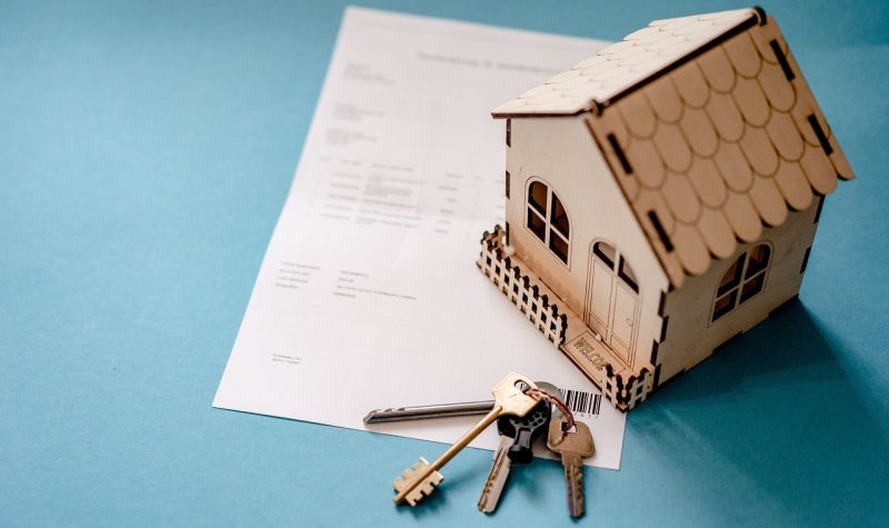 A model house and a pair of keys lie on top of a document sitting on a table top.