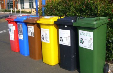 6 poubelles de couleurs différentes pour le recyclage sont garées sur un trottoir.