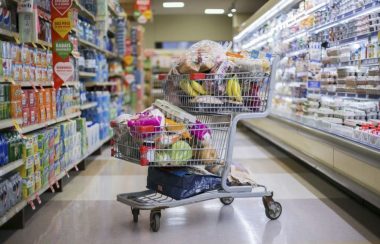 Un panier d'épicerie rempli de produits dans une allée entourée d'aliments