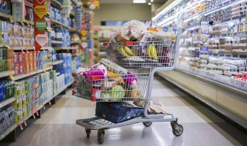 Un panier d'épicerie rempli de produits dans une allée entourée d'aliments