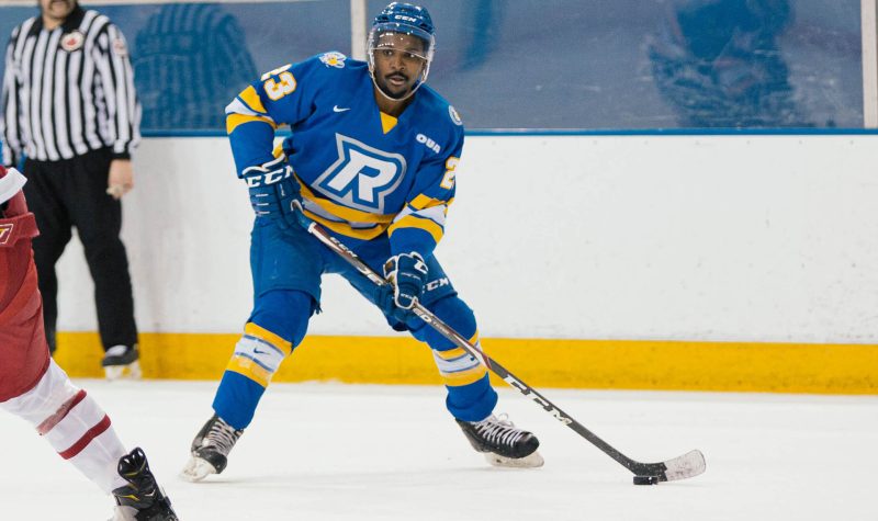 A hockey player in a blue and yellow uniform and equipment is on the ice in an indoor rink.