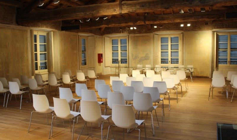 Salle de réunion éclairée avec plusieurs rangées de chaises banches