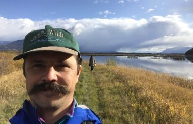 Man takes selfie in front of field and lake.