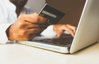person makng online purchase on laptop, holding credit card to screen