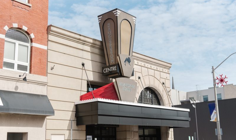 Front entrance of The Sanderson Centre. The sign displaying the name sits over top of the front entrance doors and a black awning.