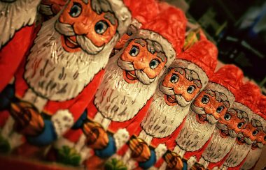 Santa Claus candies lined up in a row all wearing red hats and suits with big white beards.