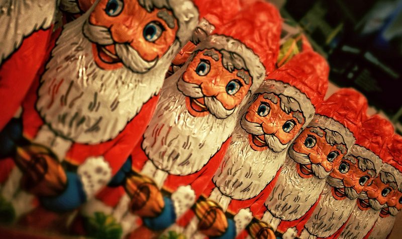 Santa Claus candies lined up in a row all wearing red hats and suits with big white beards.